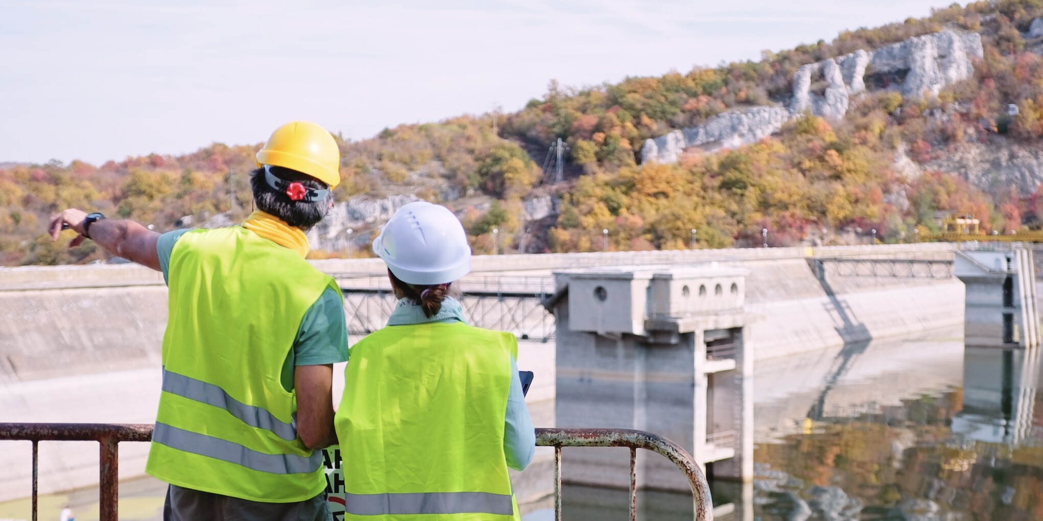 Two individuals in hard hats inspecting a dam, discussing its structure and safety features.