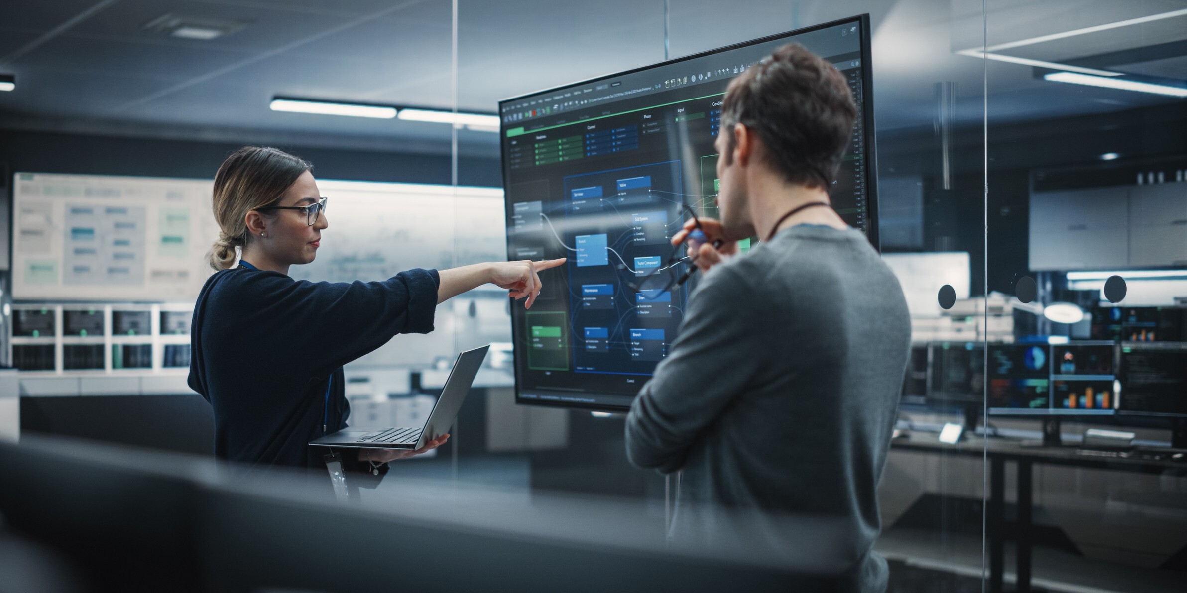 Two individuals collaborating while viewing a computer screen in a well-lit room.