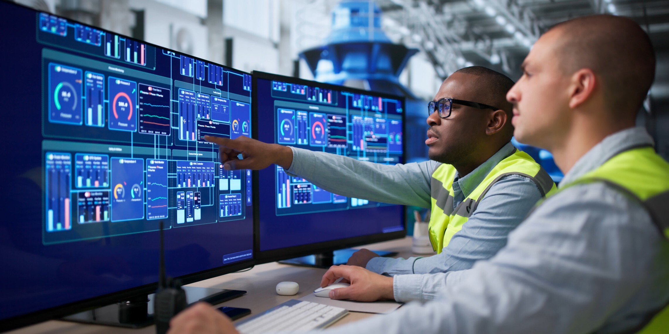 Two men in safety vests examining data on a computer screen in a work environment.